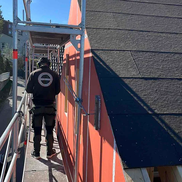 Bygningsarbeider står på stillas ved en nyoppusset bygning under klar himmel.