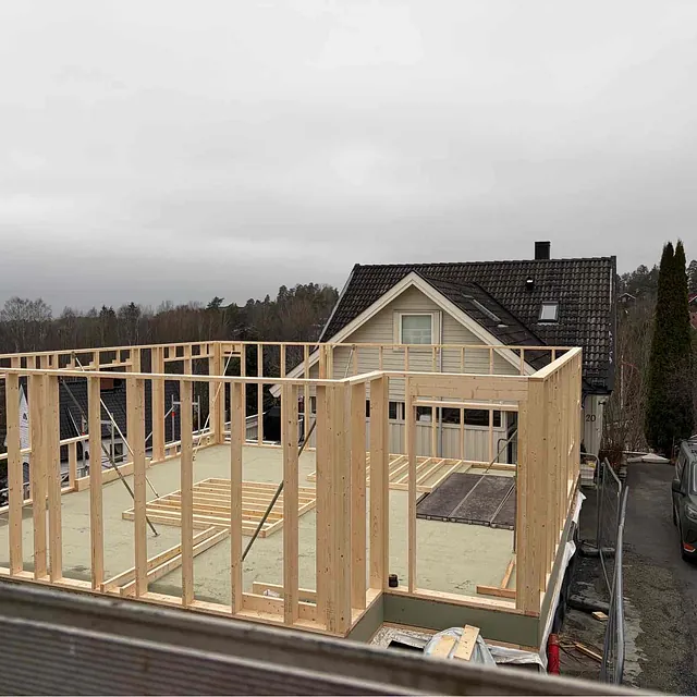 Bygging av hus med trestruktur og dekk, bakgård og biler i nabolaget under overskyet vær.