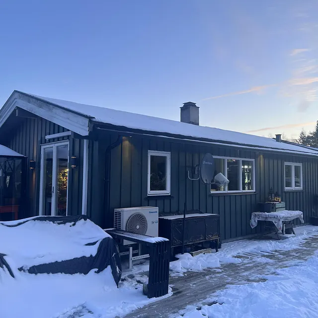 En moderne hytte med snø på bakken og klart blå himmel i bakgrunnen.